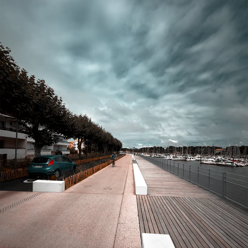 Promenade am Yachthafen von Capbreton mit Radweg, geparkten Autos und Segelbooten im Hafenbecken.