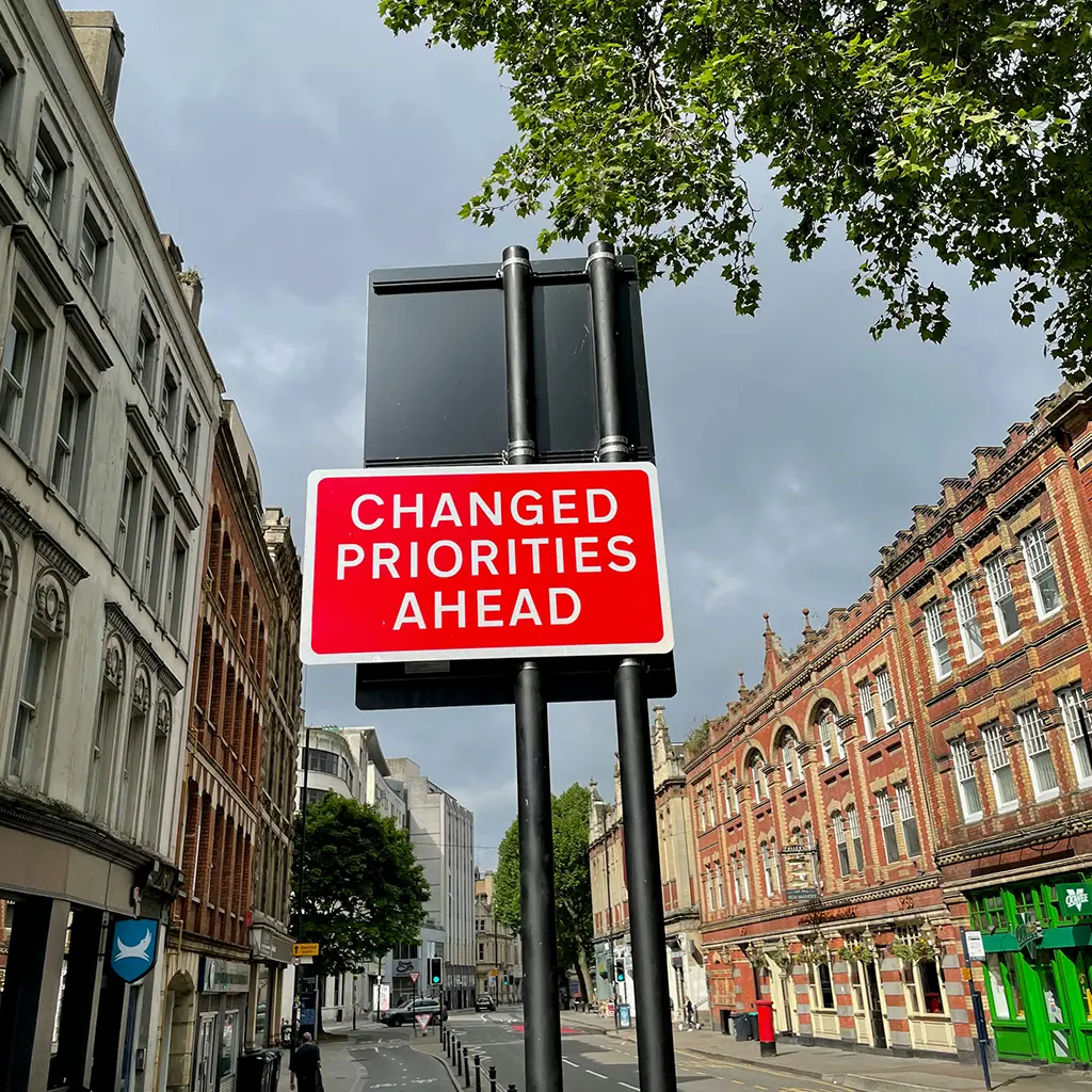 Straßenschild mit roter Aufschrift ‚Changed Priorities Ahead‘ in einer europäischen Innenstadt – Symbol für Verkehr, Mobilität und Wandel. IAA