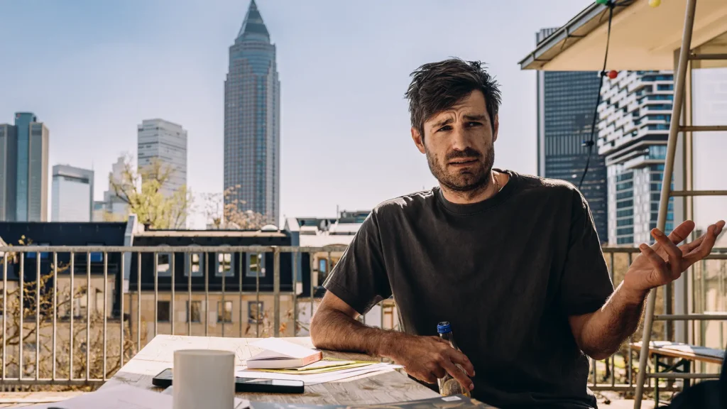 Dr. Mirko Broll auf einer Terrasse des Instituts für Sozialforschung in Frankfurt mit Skyline im Hintergrund, im Gespräch