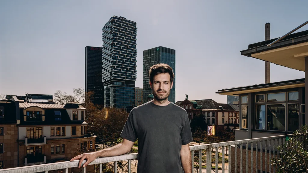 Dr. Mirko Broll auf einer Terrasse des Instituts für Sozialforschung in Frankfurt mit Skyline im Hintergrund