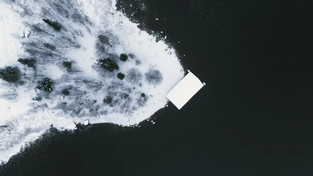 Luftaufnahme einer verschneiten, einsamen Küste mit dunklem Wasser – eine kalte, entrückte Szenerie, die die Stimmung von ‚Au Pays du Cocaine‘ widerspiegelt.
