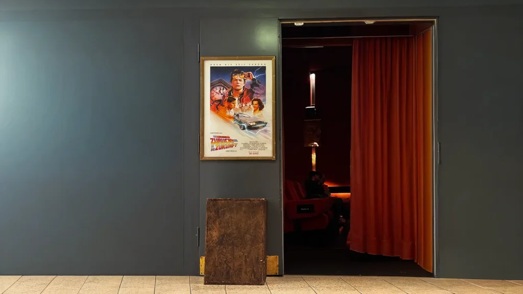 Kinosaal mit offenem roten Vorhang und Retro-Poster von ‚Back to the future‘ an der Wand. ein nostalgischer Moment zum 40-jährigen Jubiläum der Filmreihe.