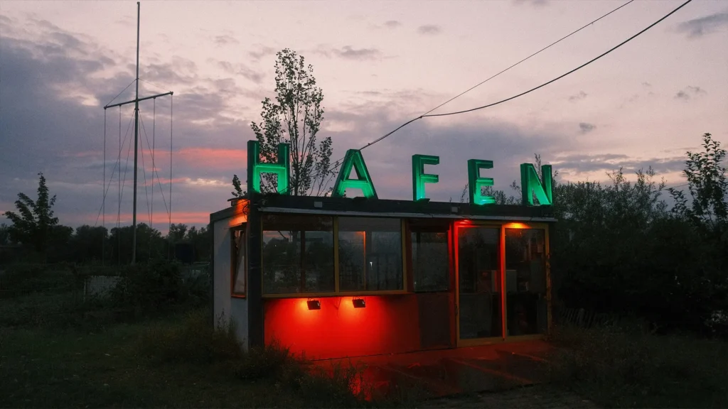 Containerbau mit grüner „HAFEN“-Leuchtschrift bei Sonnenuntergang im Offenbacher Hafenviertel. Szene-Treffpunkt im kreativen Stadtteil von Offenbach mit alternativem Flair.