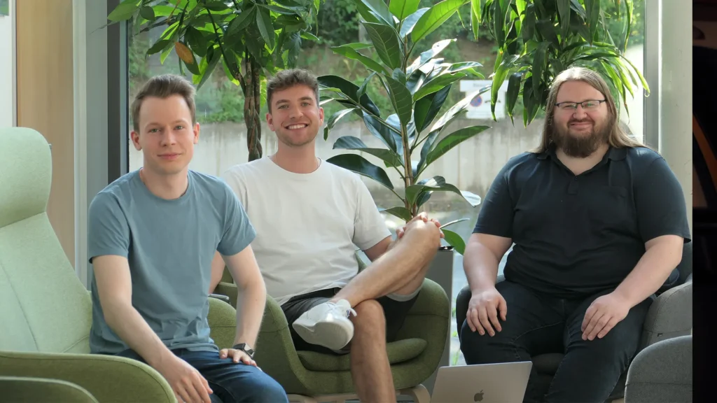 Die Gründer der Mitfahrgelegenheit App RRIVE – Jan Loescher, Felix Bonn und Marin Althuis – sitzen gemeinsam in einem modernen Büro mit Pflanzen im Hintergrund.