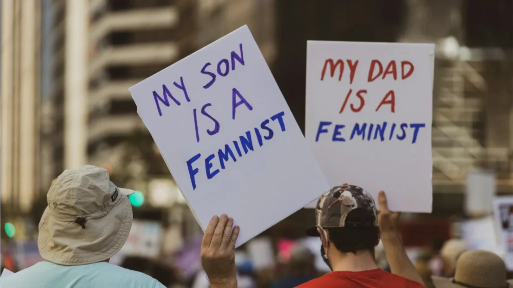Teilnehmende einer Demonstration Feministischer Kampftag halten Schilder mit der Aufschrift „My son is a feminist“ und „My dad is a feminist“.