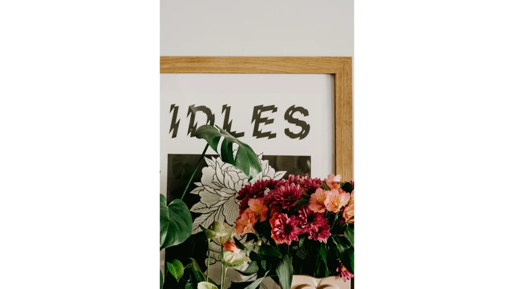 Nahaufnahme eines gerahmten Idles Posters hinter grünen Zimmerpflanzen und einem bunten Blumenstrauß.