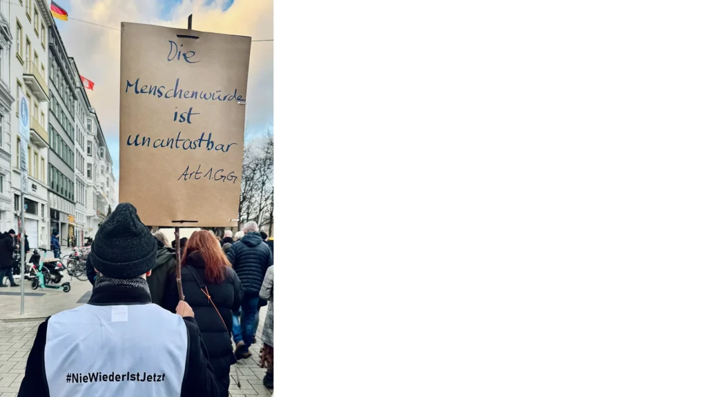 Person hält ein Schild mit der Aufschrift ‚Die Menschenwürde ist unantastbar – Art. 1 GG‘ zum Schutz der Werte des Grundgesetzes.