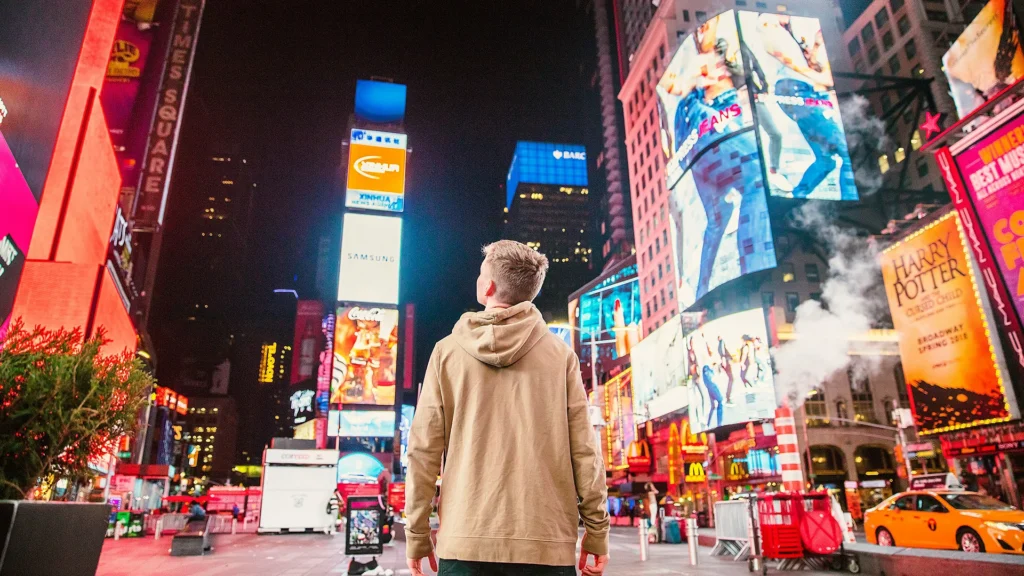 Mensch steht zwischen riesigen Werbetafeln und digitalen Anzeigen in einer Großstadt bei Nacht – Symbolbild für Werbung, Plattformmacht und digitale Aufmerksamkeit