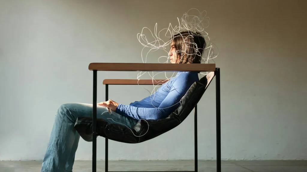 Eine Person sitzt nachdenklich in einem Sessel, während Linien Gedanken symbolisieren. Sinnbild dafür, das eigene Denken trotz KI nicht auszulagern.
