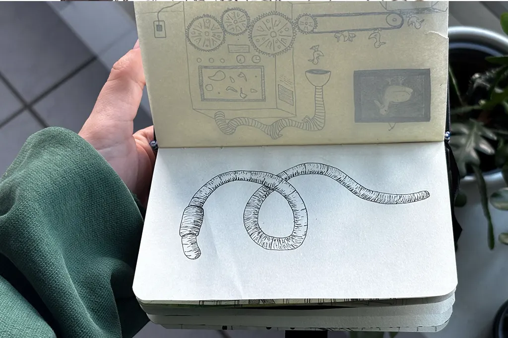 Inktober: Zeichnen mit Tinte. Ein Regenwurm mit gerillten Ringen liegt in einer Schlaufe auf der Seite. Auf der Vorseite schimmert eine Zeichnung mit Zahnrädern und Fließband durch. Inktober-Zeichnung von @kallarized